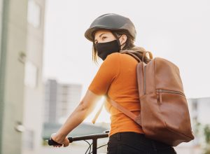 Young adult riding a bicycle through the city wearing face mask against COVID-19