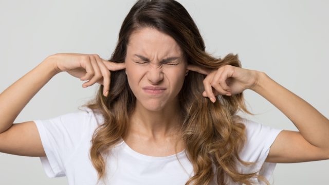 woman in a white shirt plugging her fingers in her ears