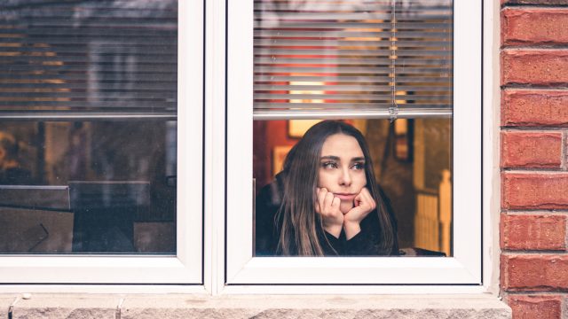 A young woman looks out her window with a distressed look on her face due to coronavirus lockdowns