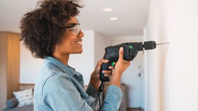 Young black woman drilling wall