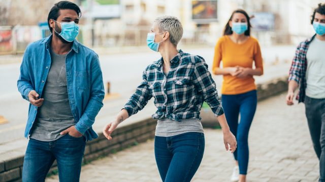 A group of young people walking down the street while wearing face masks.
