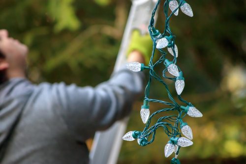 Man using ladder to hang Christmas lights