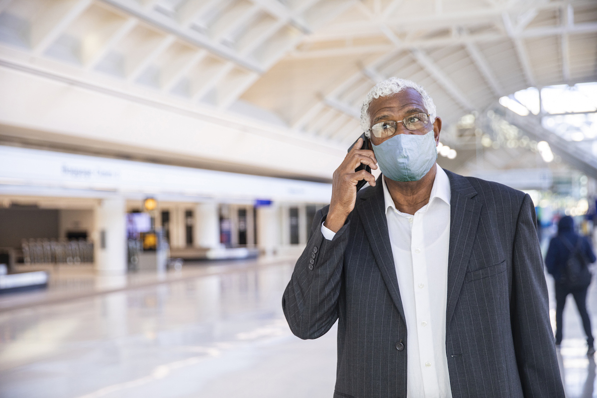 A Senior man using his phone in the airport while wearing a face mask during COVID