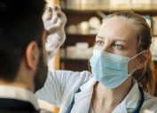 Female healthcare worker wearing surgical mask examining male patient. Doctor checking eyes of mid adult man. They are at a hospital.