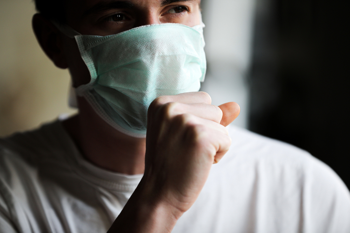 young man coughing while wearing a mask