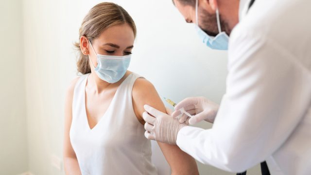 Closeup of a nervous woman and her doctor wearing face masks and getting the COVID vaccine