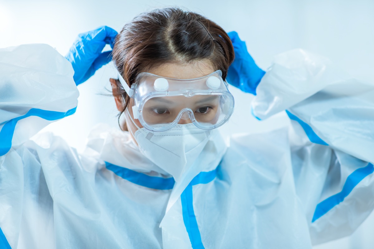 young female doctor adjusting her goggles while wearing face mask and blue nitrile gloves