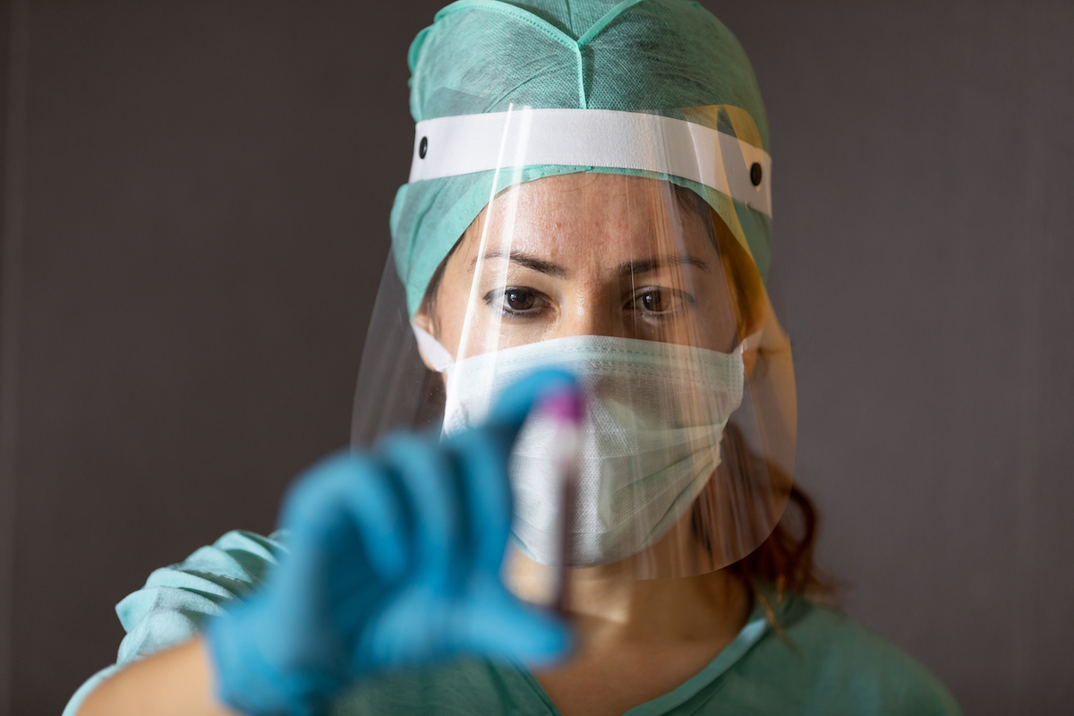 doctor with mask and face shield holding up vial of blood