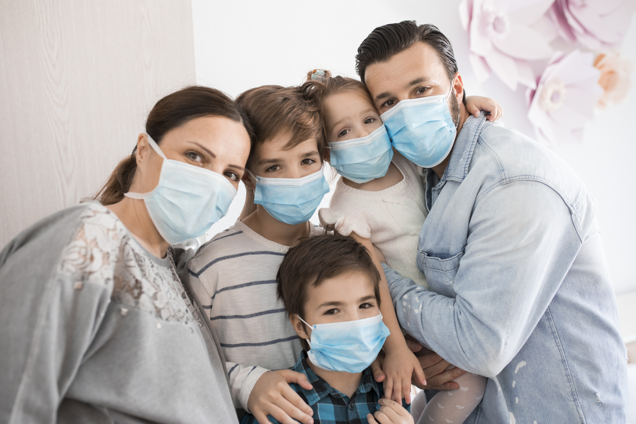 A family of a mother, father, and three children all wearing face masks while indoors.