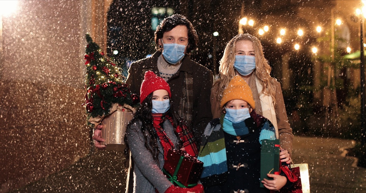 man, woman, and children wearings masks outside in the snow and holding Christmas gifts