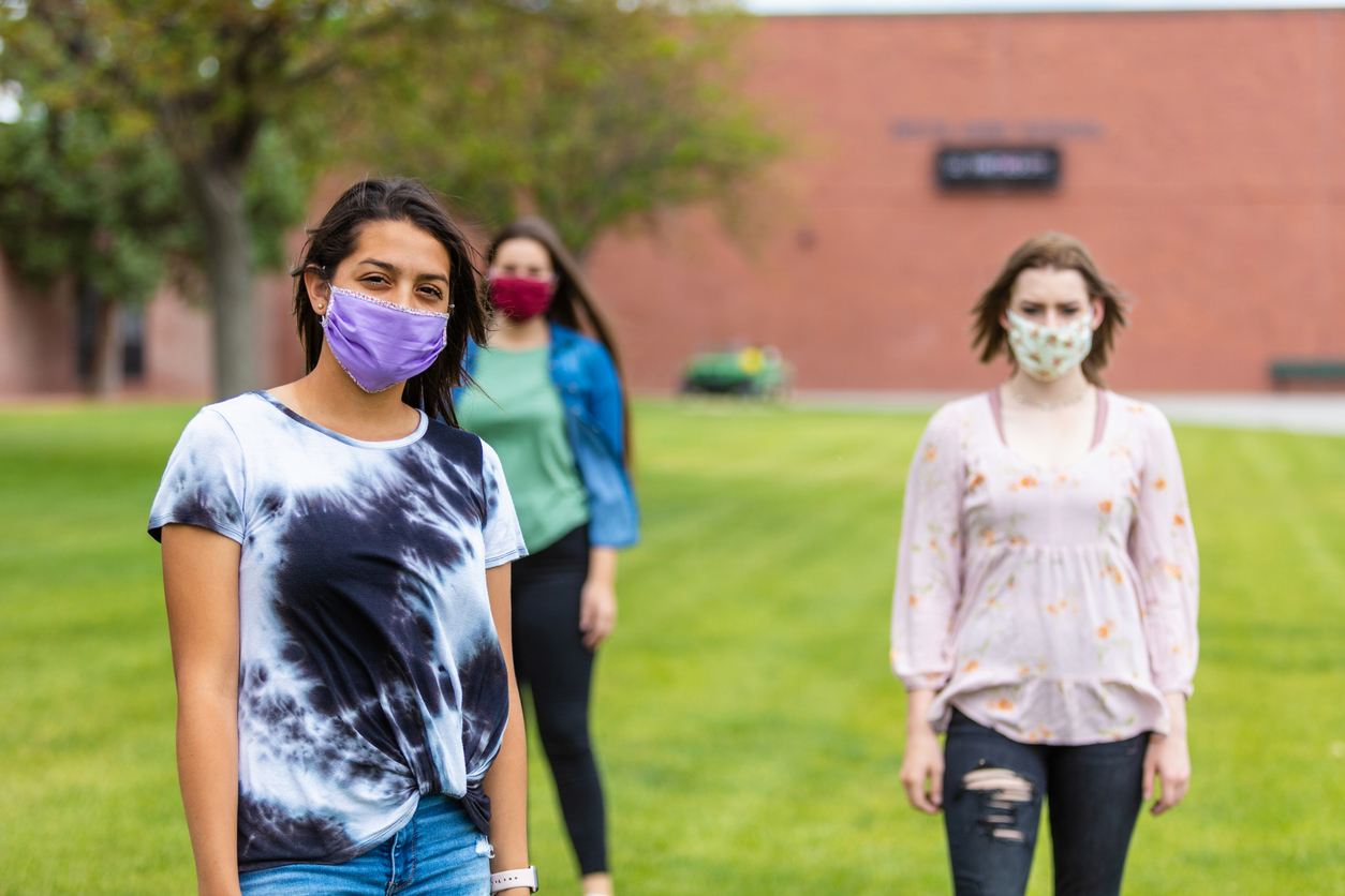 A group of three female friends wearing face masks while socially distanced outdoors.