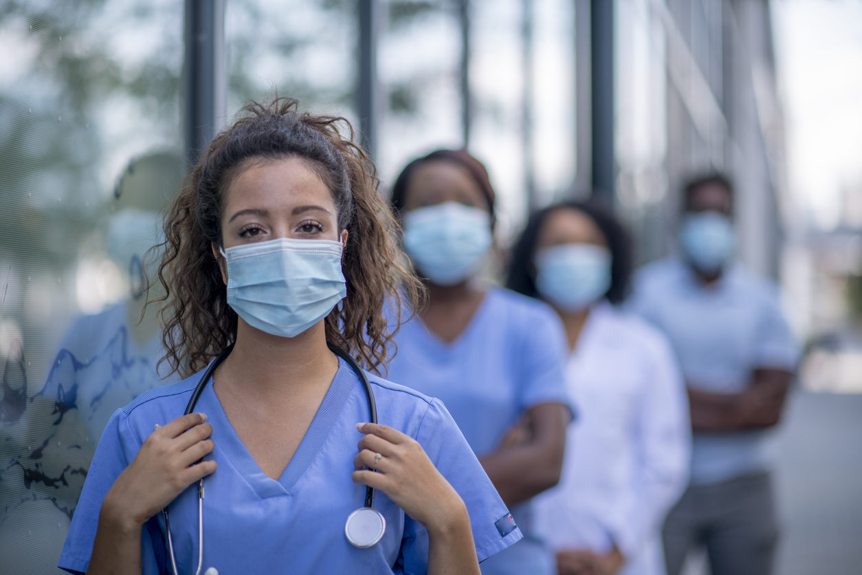 A group of doctors and nurses wearing face masks stand socially distanced while outside.