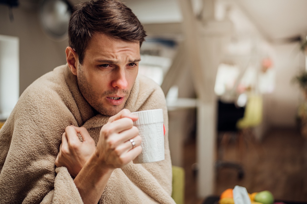 Young man shivering under the blanket and drinking tea