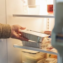 Man's hand taking wrapped up food out of refrigerator.