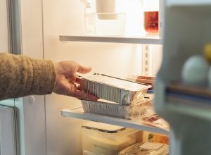 Man's hand taking wrapped up food out of refrigerator.
