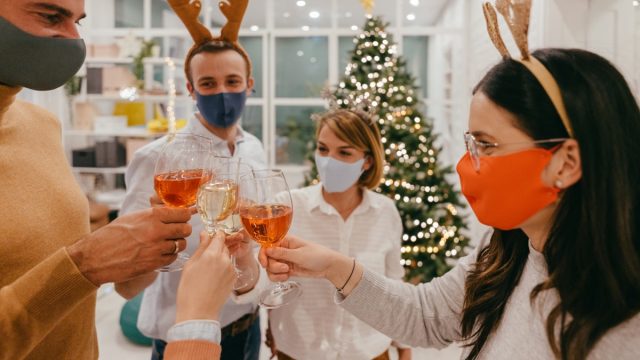 Photo of a group of coworkers celebrating Christmas together in their office, wearing protective masks and keeping distance