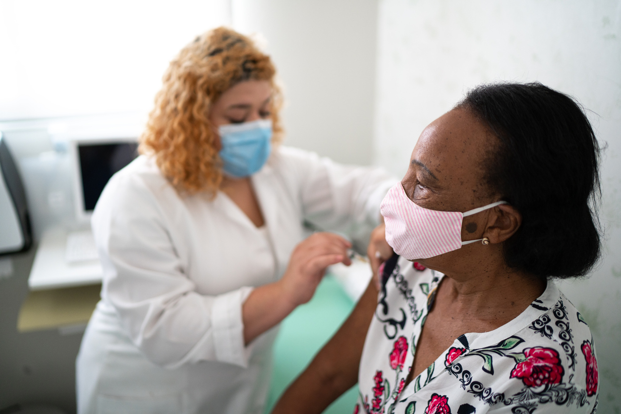 A senior woman wearing a face mask receives a COVID vaccine from a female healthcare worker.