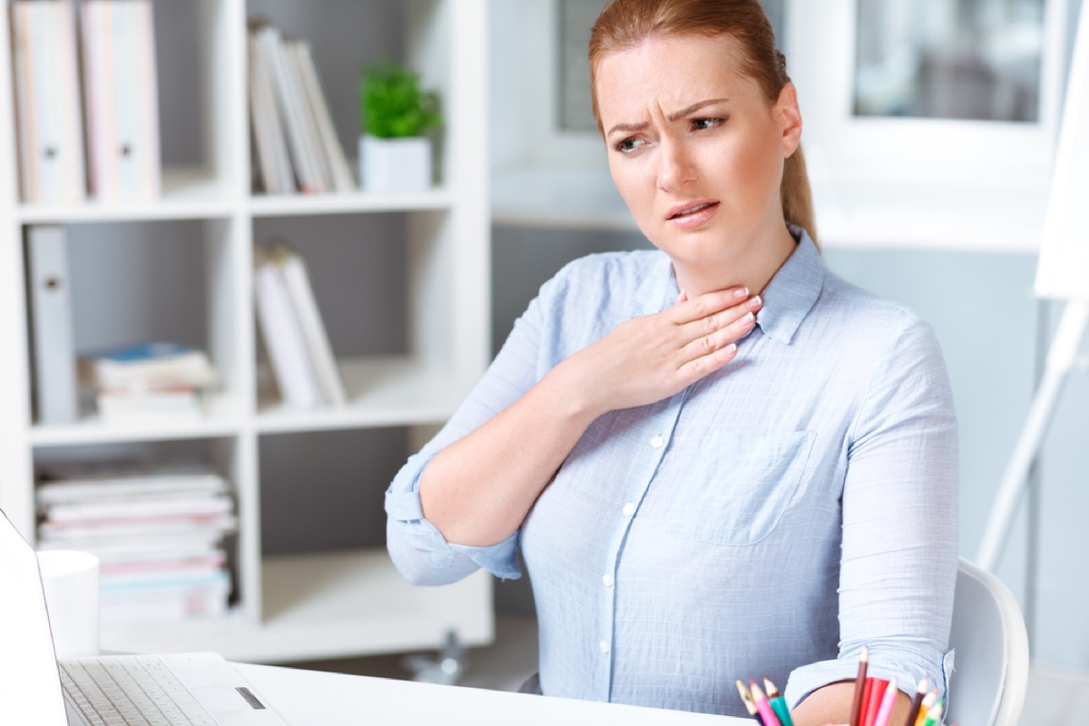 woman touching her throat and looking worried in an office
