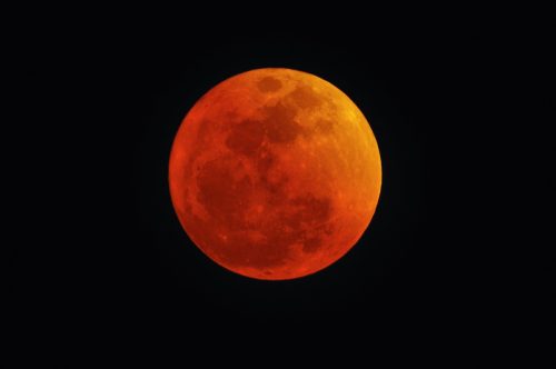 A red and orange moon in the dark night sky