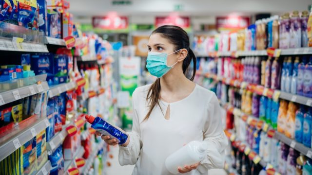 woman wearing white blouse and surgical mask buying cleaning supplies at grocery store