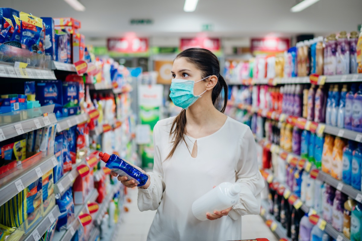 woman wearing white blouse and surgical mask buying cleaning supplies at grocery store