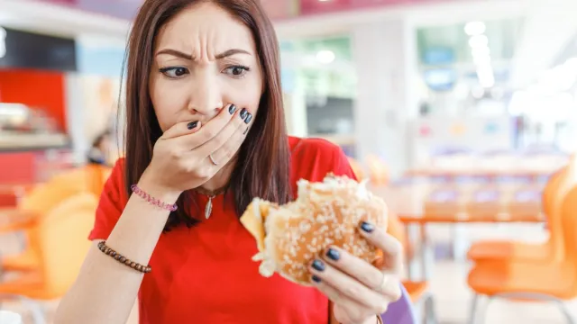 young woman covering mouth and holding hamburger
