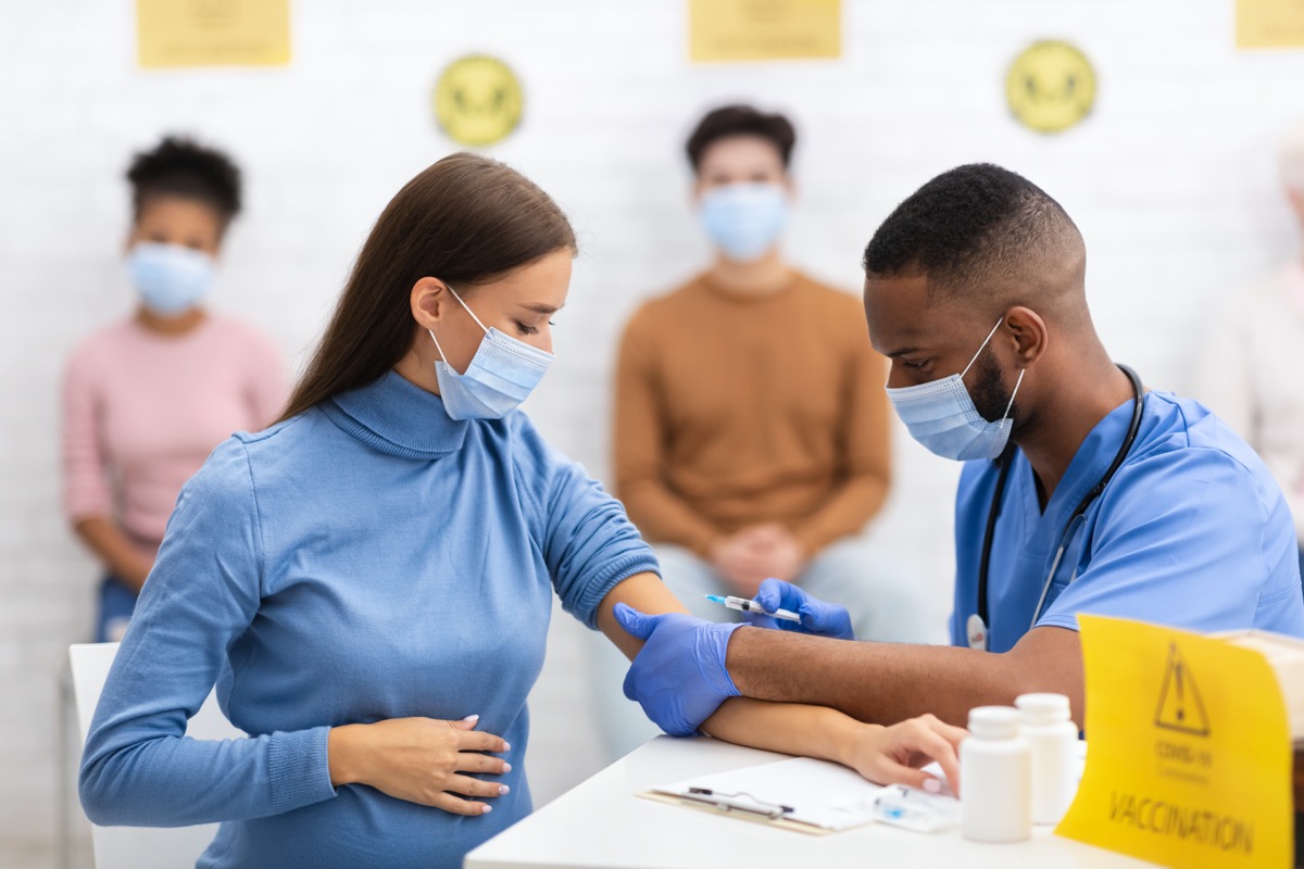 woman in surgical mask getting covid vaccine from medical professional in blue scrubs and surgical mask