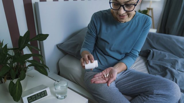 A senior woman sitting in bed prepares to take two supplement pills.