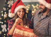 man giving woman gift and they're both wearing santa hats