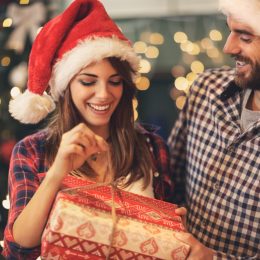 man giving woman gift and they're both wearing santa hats