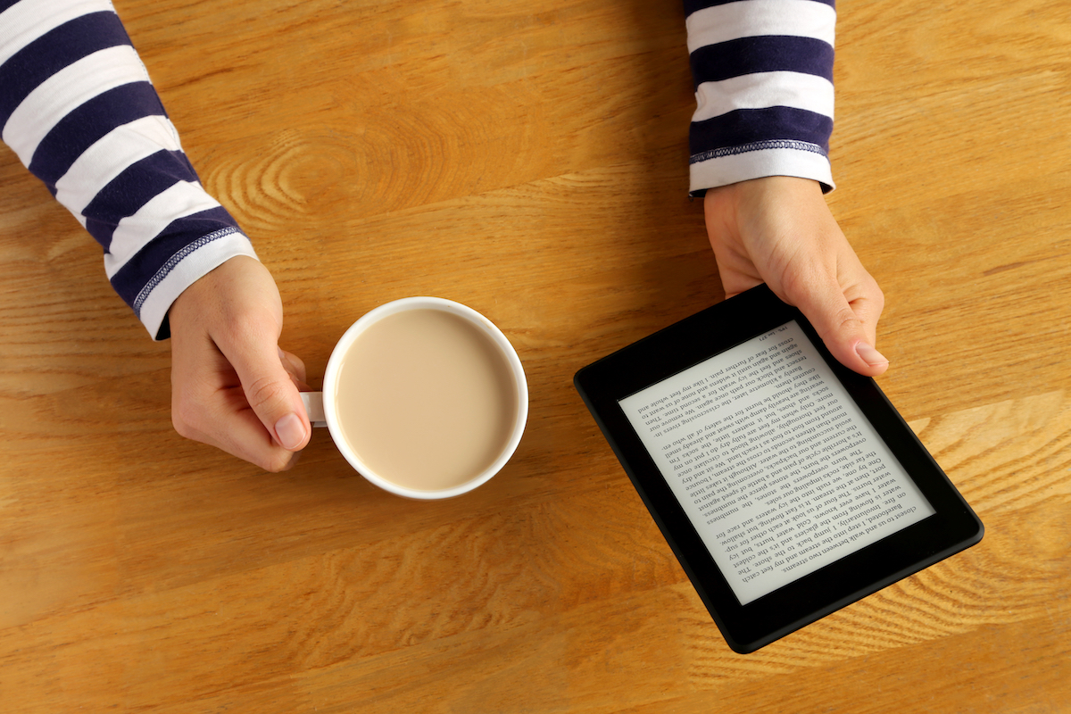 Woman reading a novel on a tablet and drinking her coffee.