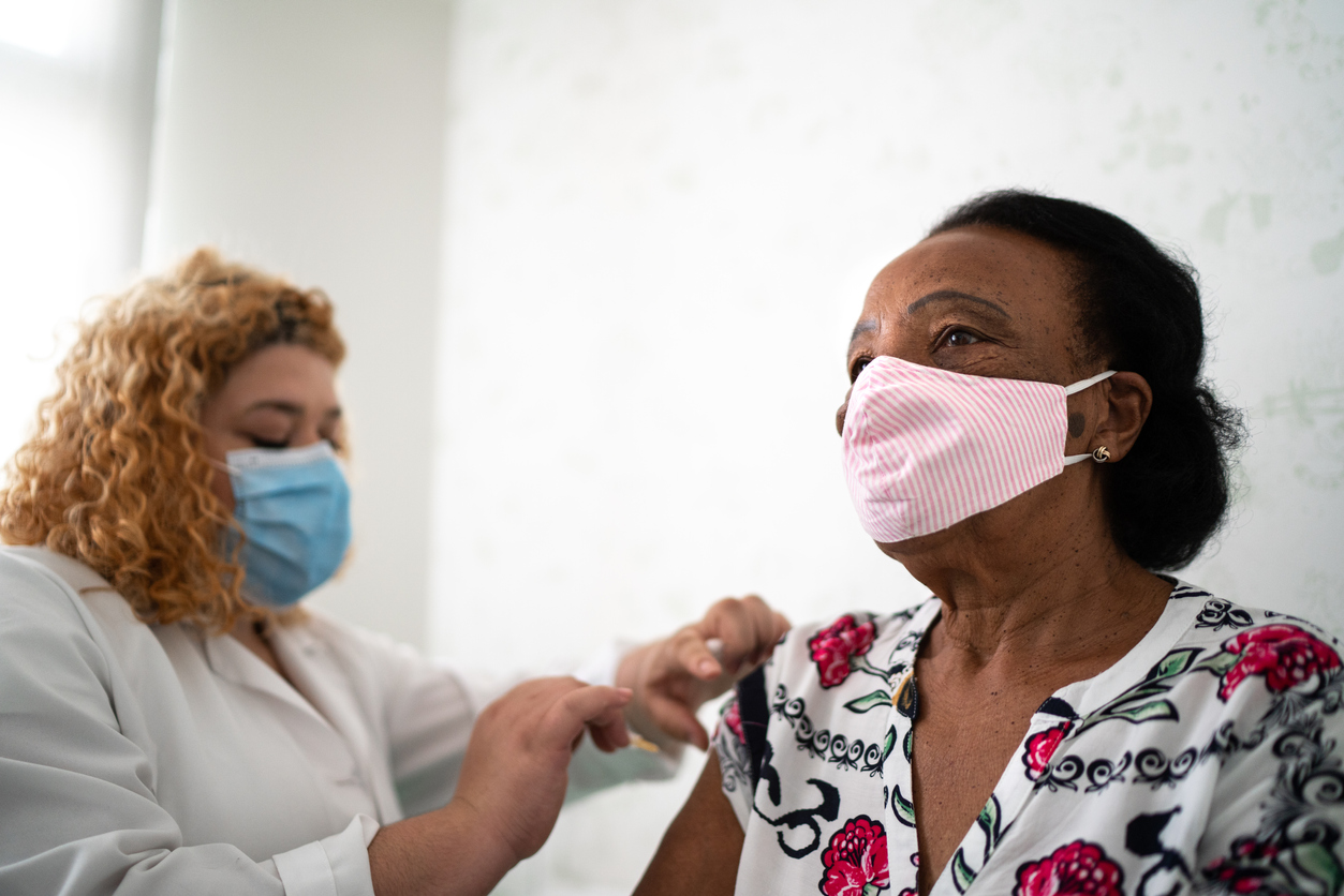A senior woman wearing a face mask receives a COVID-19 vaccine from a female healthcare worker.