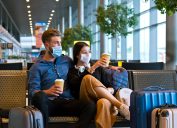 A young couple wearing face masks while sitting in a transit lounge waiting to travel during the holidays.