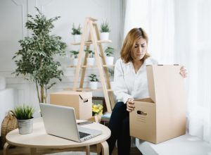 young woman opening cardboard box and looking upset with plants behind her