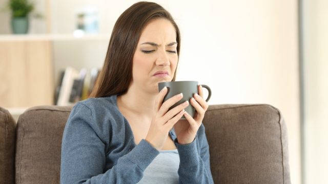 young woman making upset or disgusted face while looking at her gray teacup