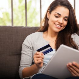 young woman smiling while holding tablet and credit card
