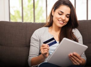 young woman smiling while holding tablet and credit card
