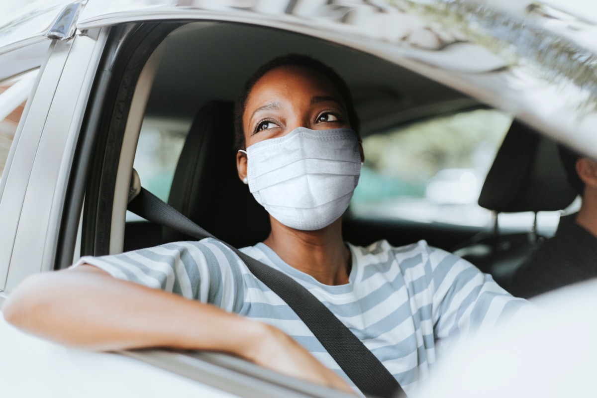 young woman wearing mask in car with window rolled down