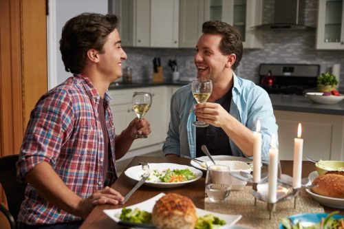 Zwei Männer, die ein romantisches Abendessen haben und sich gegenseitig anstoßen
