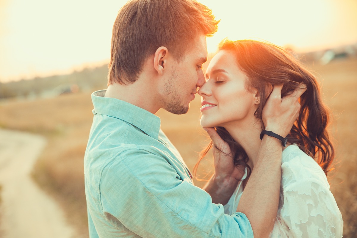 Man and woman about to kiss in field at sunset
