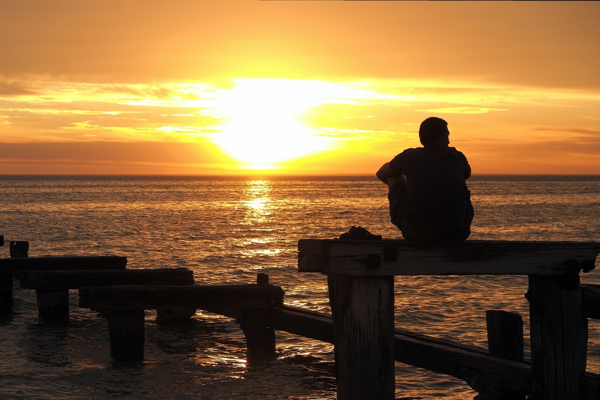 Man sitting on dock at sunset looking at water