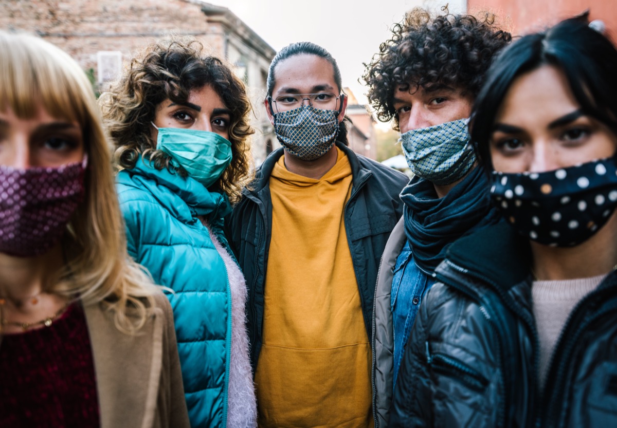 crowd of citizens in city street covered by face mask looking at camera - New normal lifestyle concept with people worried about pandemic virus - Focus on guy in the middle