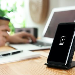 black contact phone charger on wooden desk next to person working on laptop