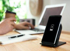 black contact phone charger on wooden desk next to person working on laptop