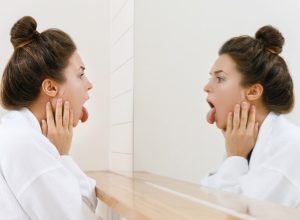 Young woman is looking on her tongue in the mirror