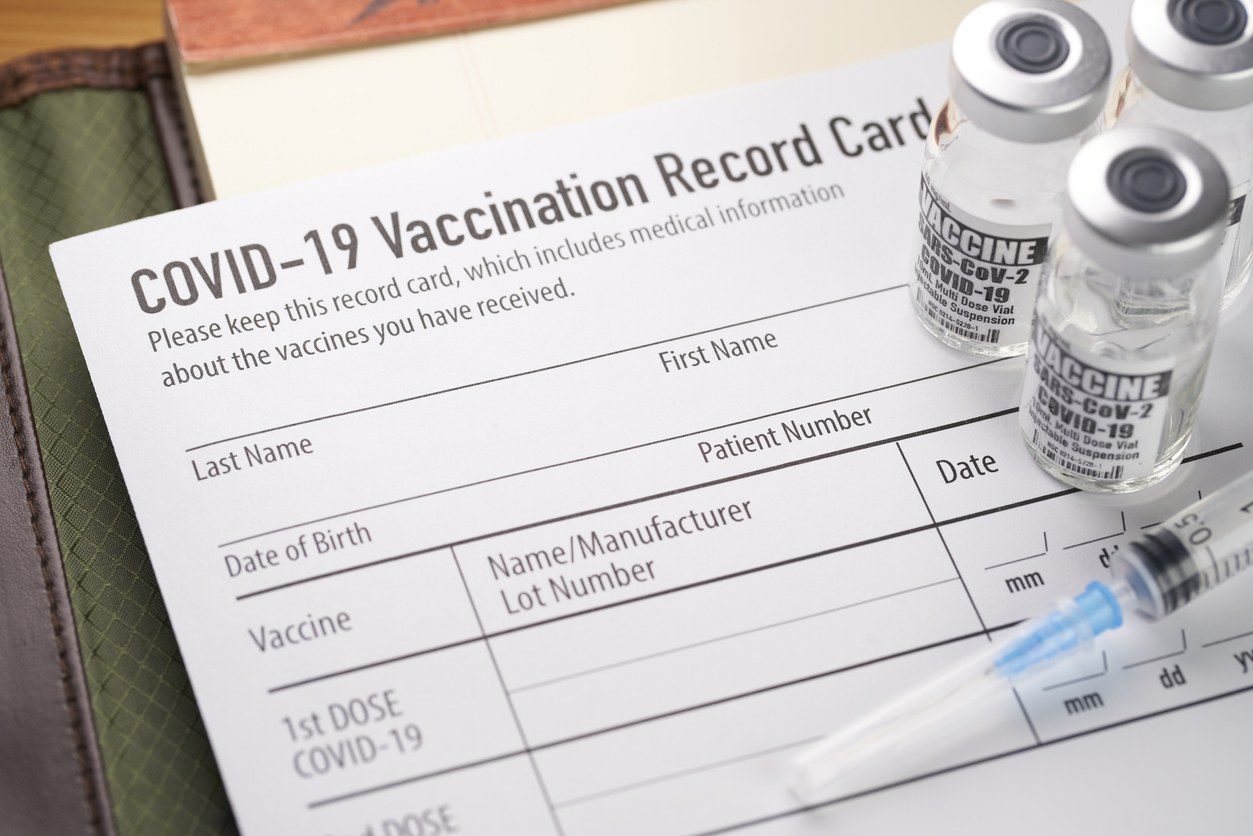 Vials of COVID-19 vaccine and a syringe sit on top of a vaccination date record card.