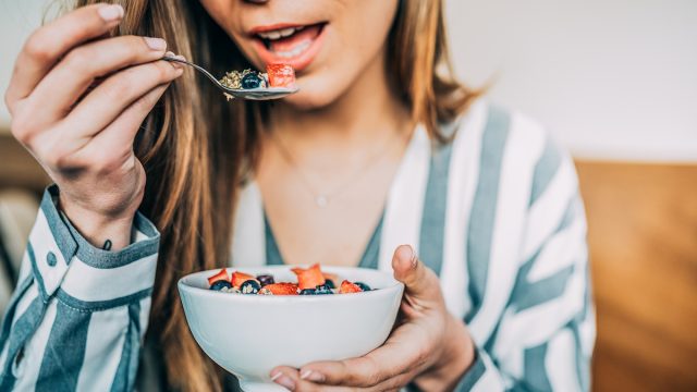 close up of woman eating oat and fruit in bowl for breakfast