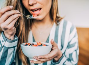 close up of woman eating oat and fruit in bowl for breakfast