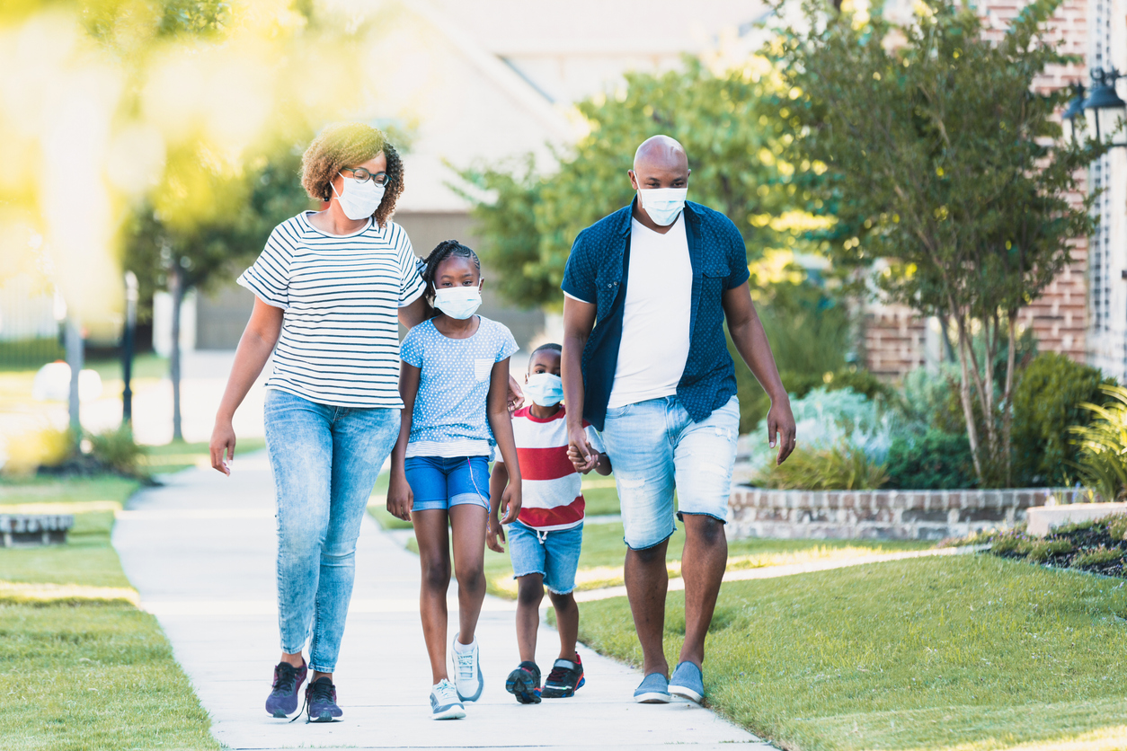 A Black family of four walking on a sidewalk while wearing face masks.