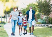 A Black family of four walking on a sidewalk while wearing face masks.
